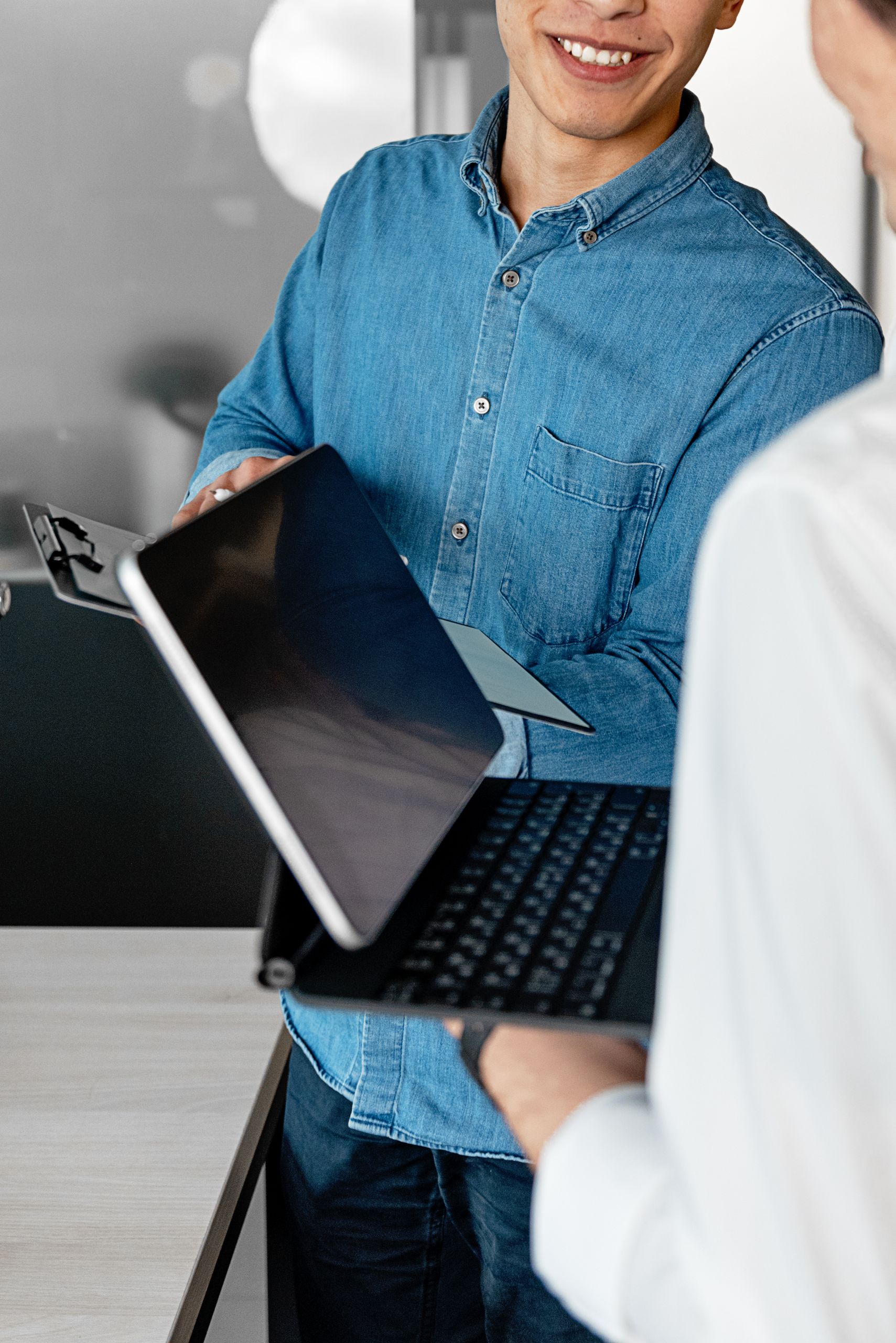 Home Two adults working together, exchanging a tablet and laptop in an office.