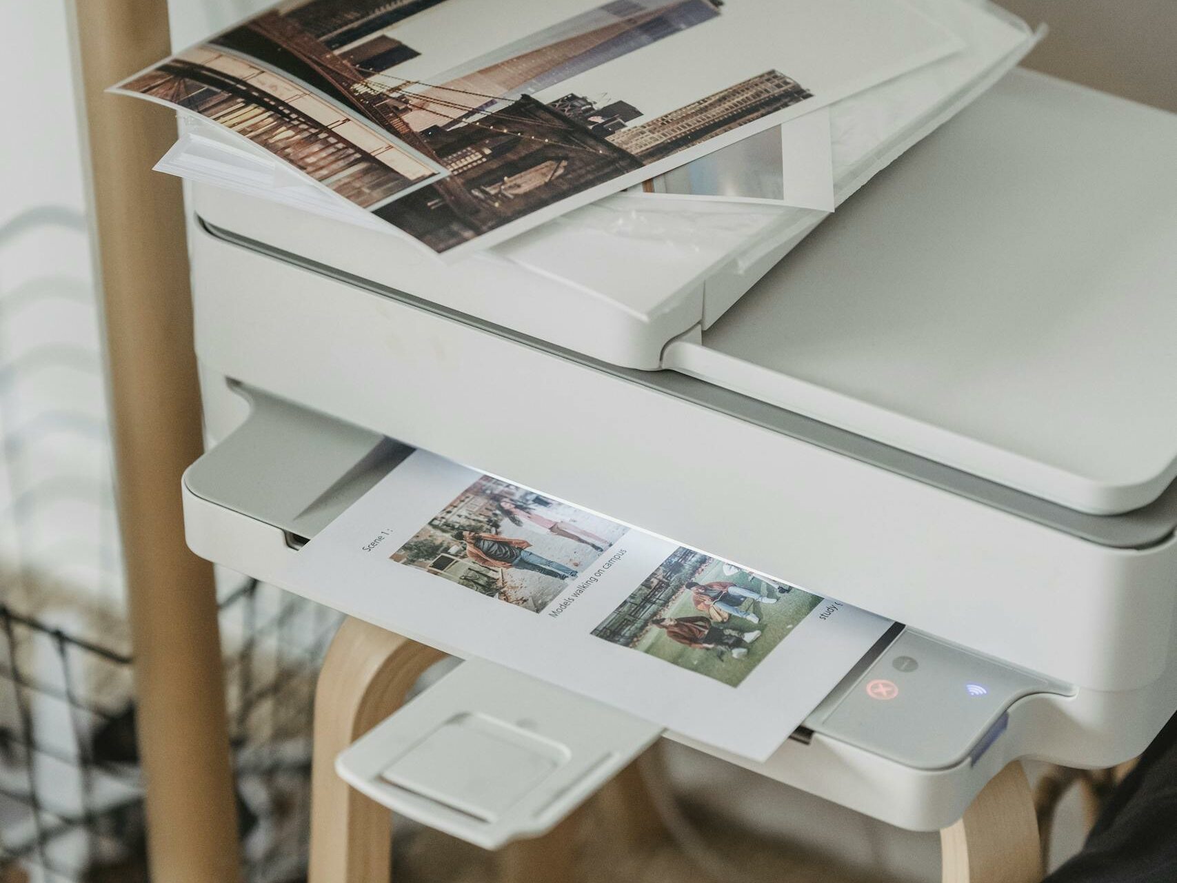A cozy home office corner with a printer, coffee cup, and printed photos on a wooden table.